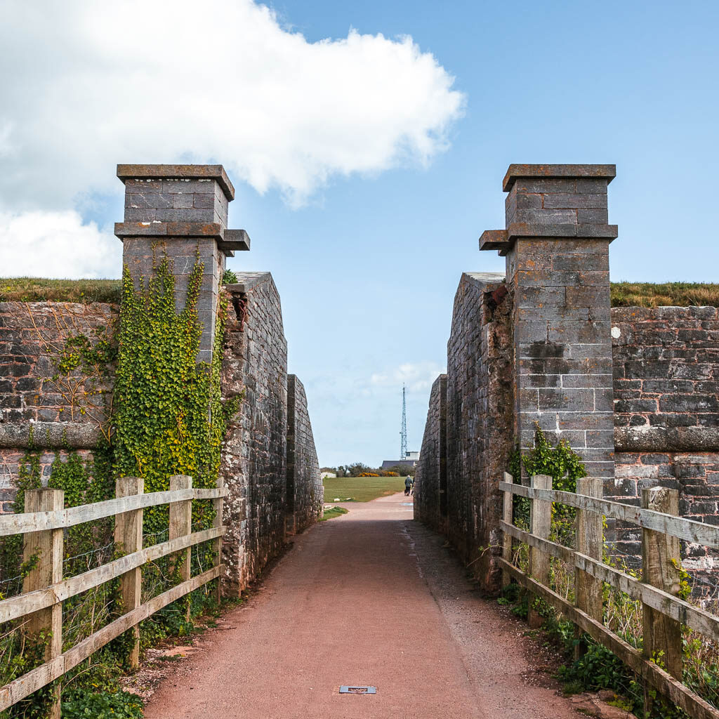 A path leading through the stone and brick wall and pillars towards Berry Head.