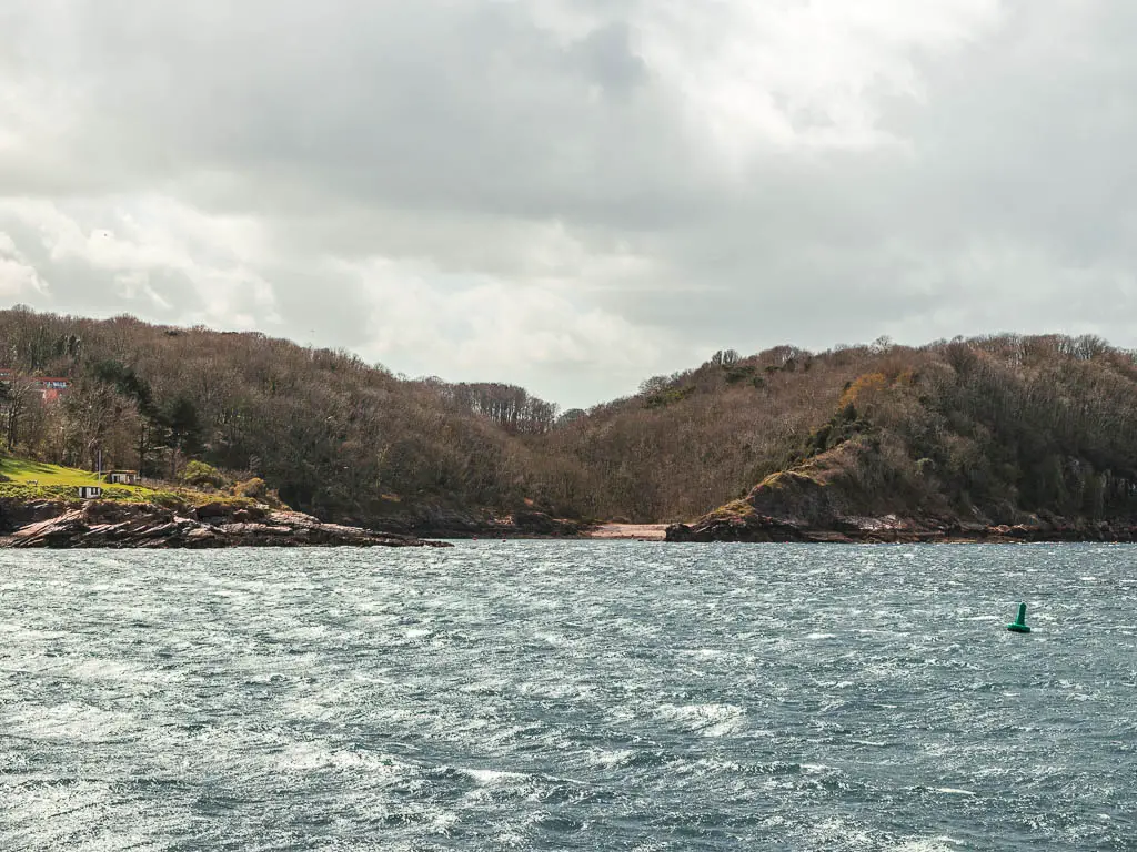 Looking across the choppy sea to a small secluded beach cove within the trees.