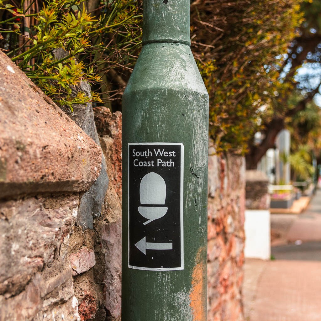 A green lamppost with a back and white sticker saying 'south west coast path'.