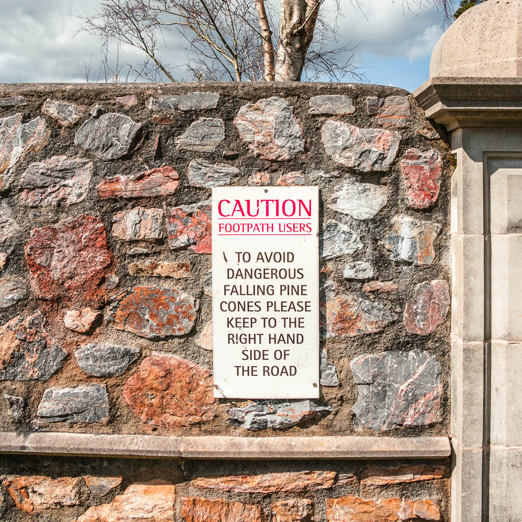 A warning sign of pines cones falling on the stone wall.