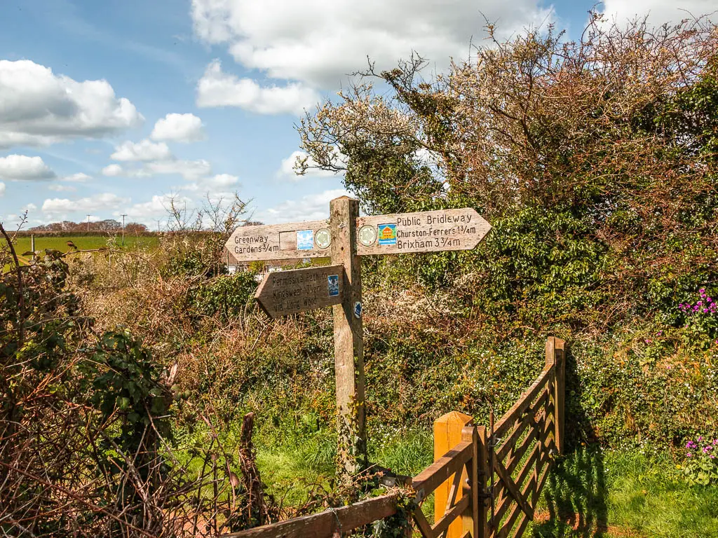 A wooden trail signpost next to a wooden fence and gate on the Kingswear to Greenway and Dartmouth to Dittisham walk.