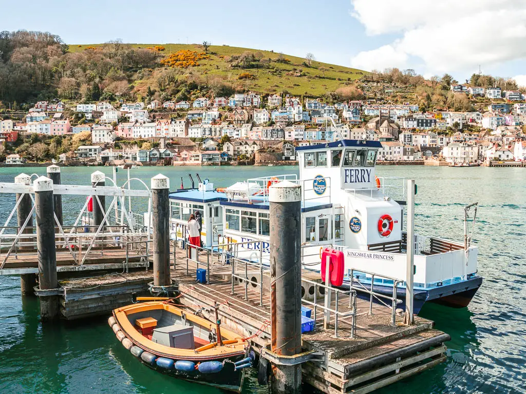 A pier with a white ferry boat docked and Dartmouth on the other side of the river.