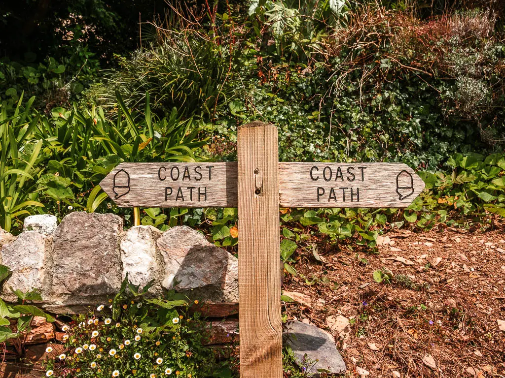 A wooden trail signpost saying 'coast path' pointing left and right at the start of the walk from Kingswear to Brixham.