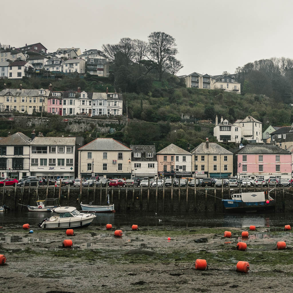 Looking across the harbour river bed to rows of pastel coloured houses in Looe, at the start of the walk to Polperro. Its a grey misty day.