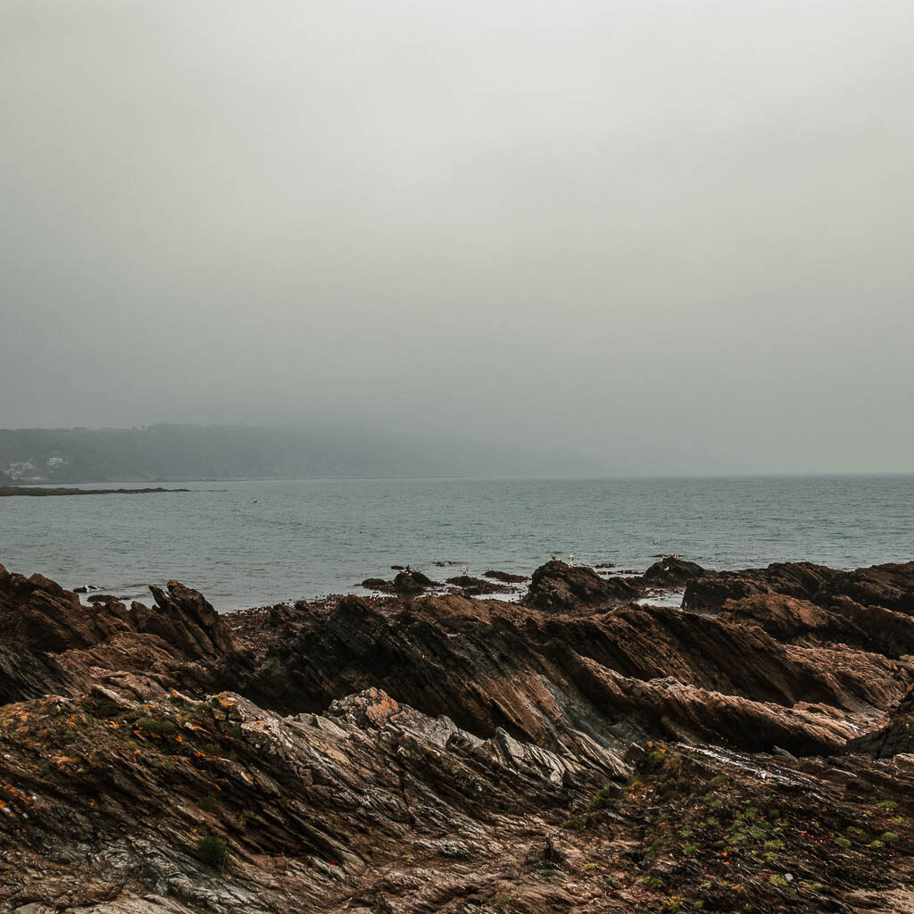Jagged rocks in front of the sea on a grey misty day.