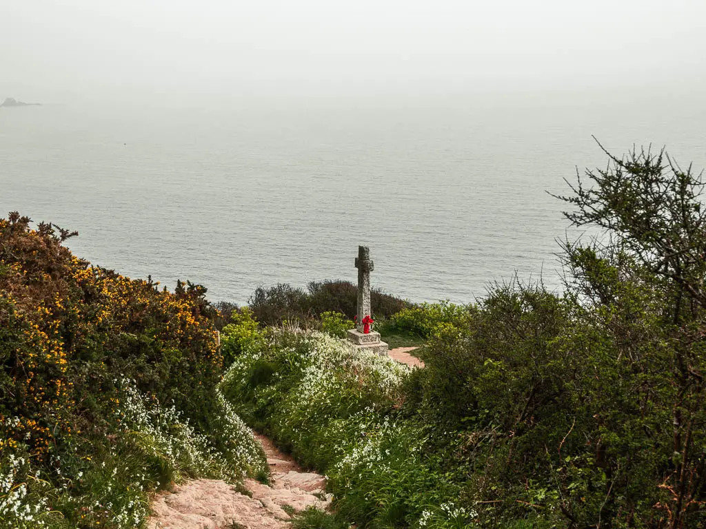 Looking down the trail lined with bushes towards a cross, with the sea as a backdrop, on the coastal walk from Looe to Polperro.