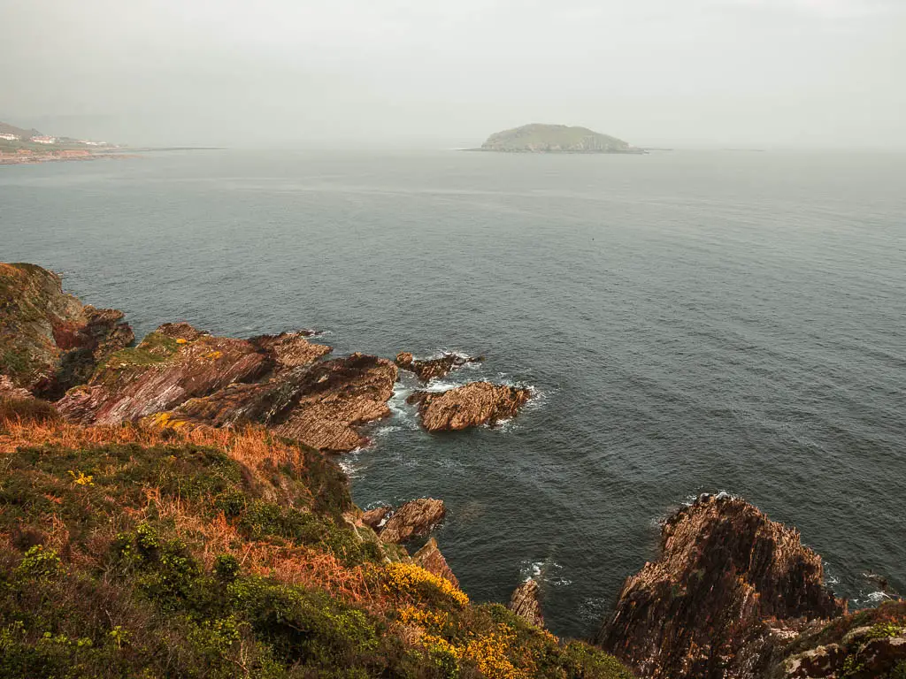 Looking down at the rocky coastline where it meets the sea, with Looe Island ahead, on the coastal walk to Polperro.