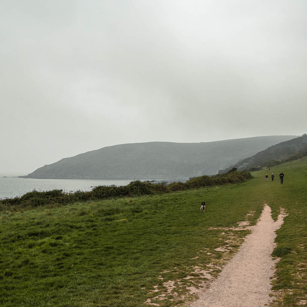 A large slanting grass hill, with a path running through it. There is a peninsular visible in the sea in the distance.
