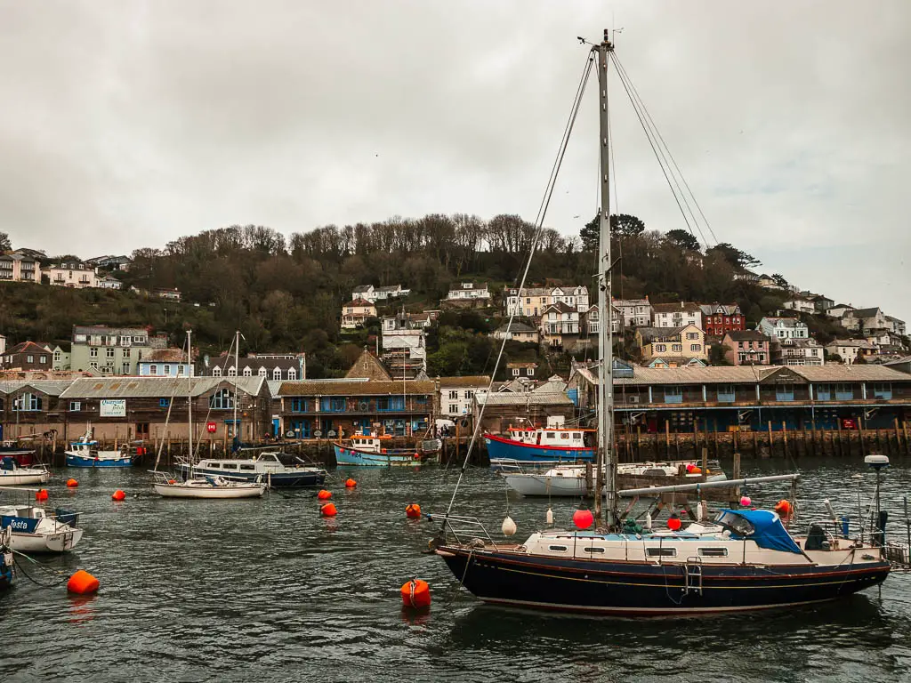 Looking across the Looe Harbour at high tide, with a few boats moored and houses on the hill on the other side.