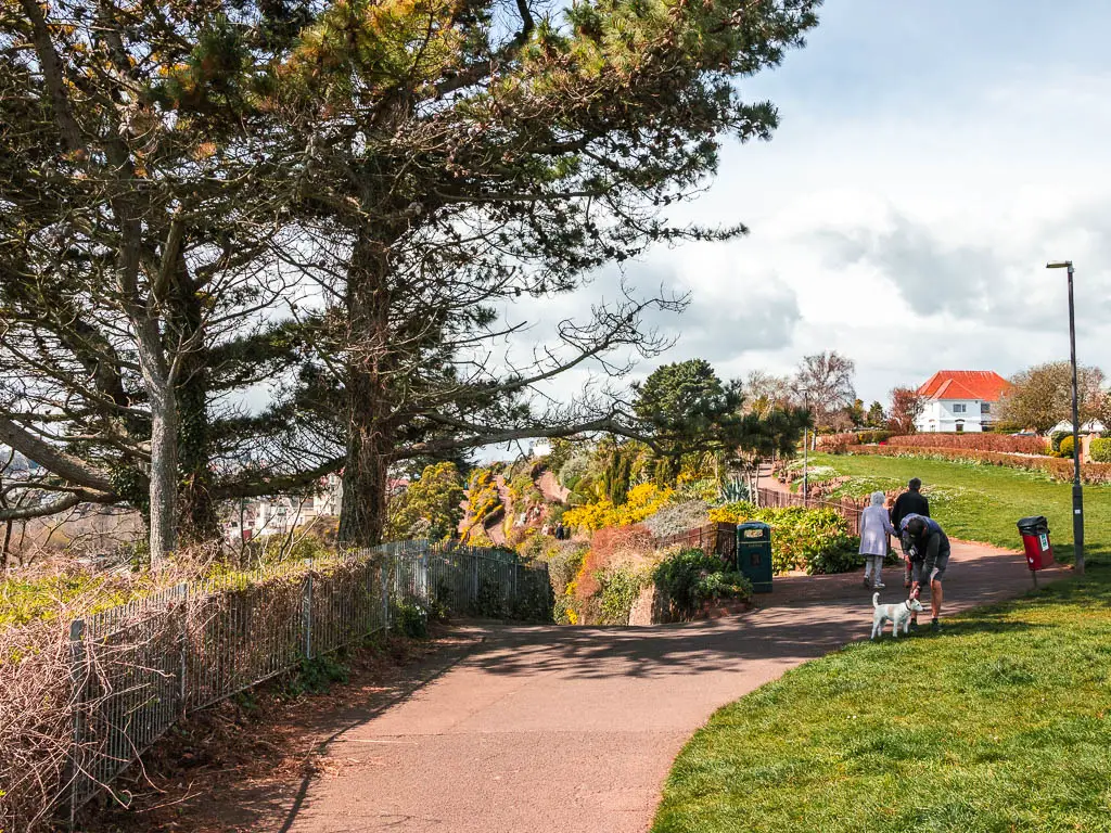 A path with a green on the right and a few people and a dog on the path.