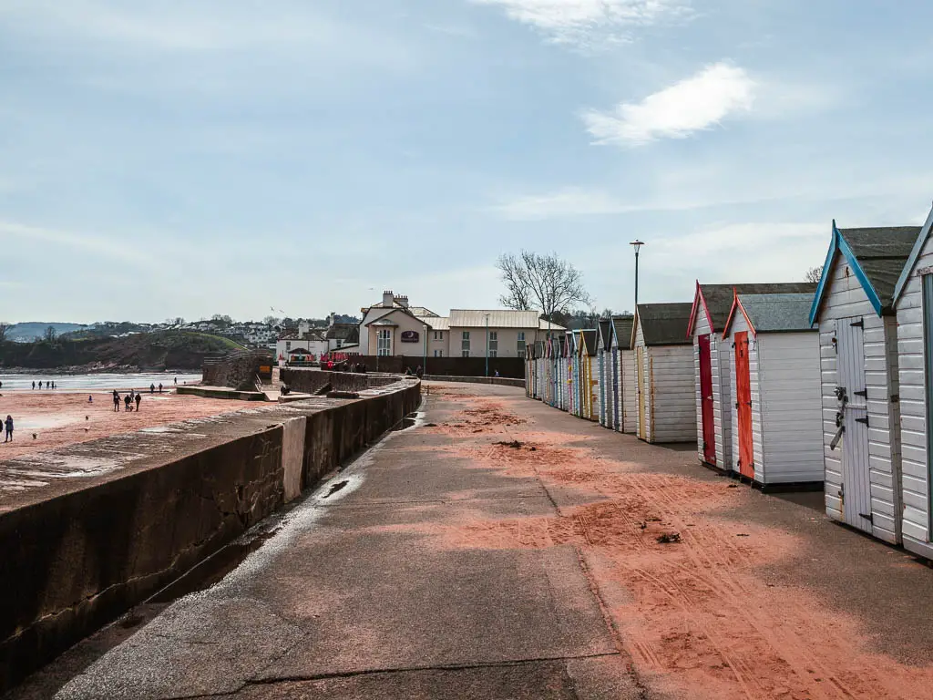 The promedade with white beach huts with colourful doors lining the right side of it. 