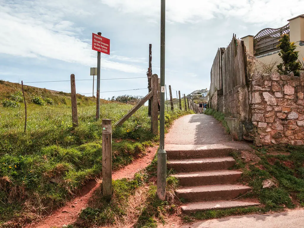 A few steps leading up to the path, with a stone wall to the right and grass to the left.