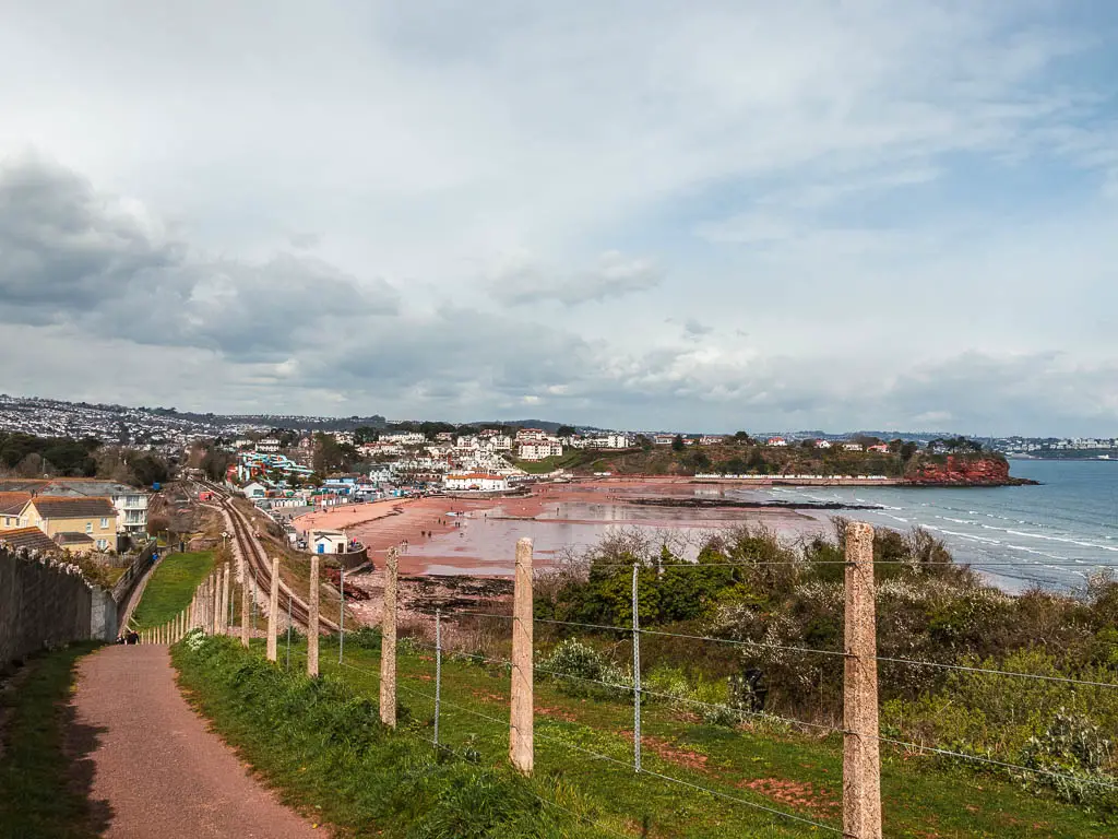 A path on the left and green and wire fence to the right, looking down towards Goodrington Sands and the railway line.