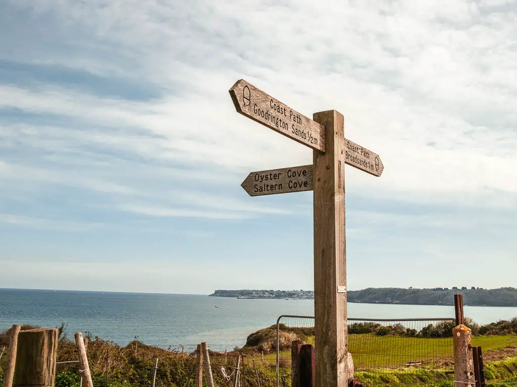 A wooden trail signpost marking the coast path on the walk from Paignton to Brixham. The blue sea is visible in the distance. 