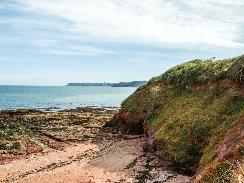 Looking down to the sandy beach cove with a moss covered cliff on the right on the walk to Brixham from Paignton. 