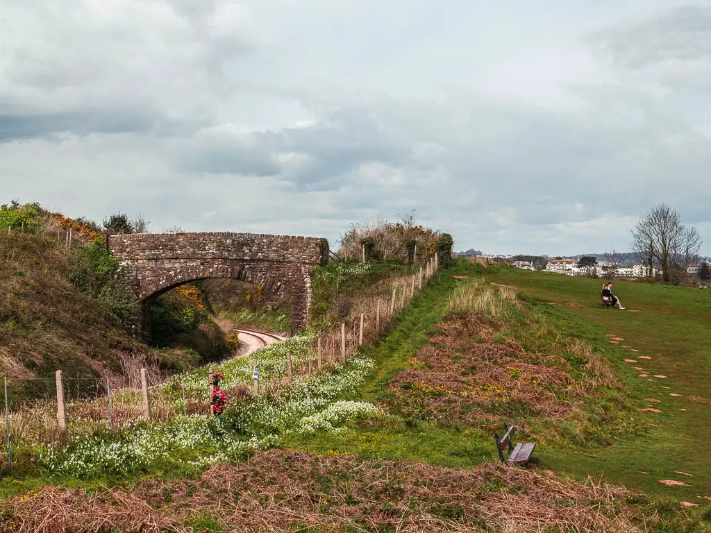 Looking across the green on the right and stone bridge on the left over the railway line.