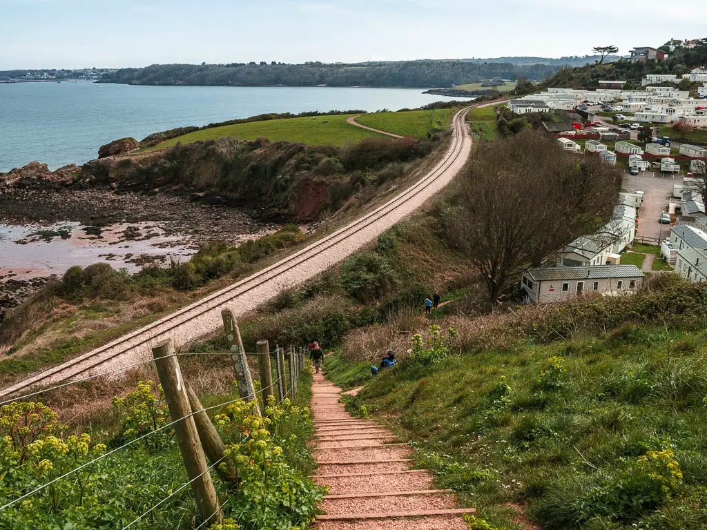 Steps leading down towards the railway line with the see ahead in the diatcue on the other side of the green grass clifftop.