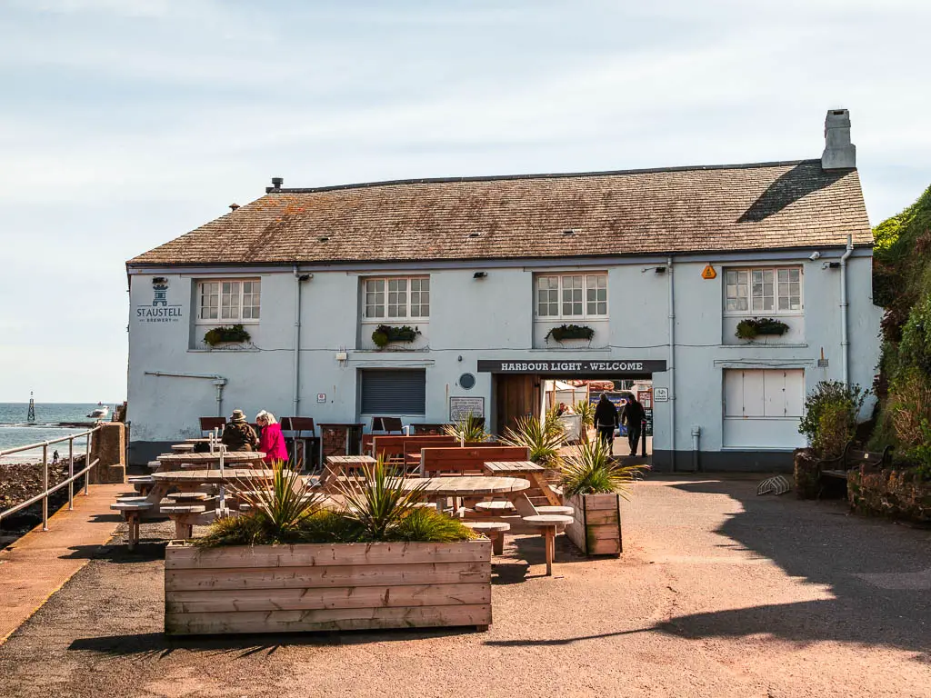 The Harbour light building in Paignton. There are a few picnic benches outside with a couple of people sitting on them.