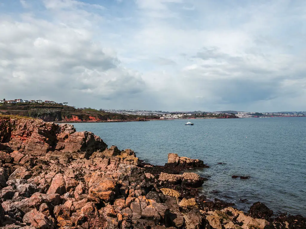 Looking across the rocks to the blue sea and towns visible on the land in the distance. 