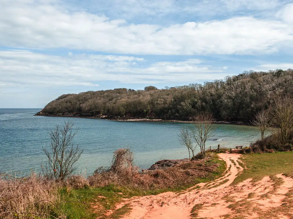 Looking down the wide rugged trail as it leads to the blue sea and a tree covered peninsula ahead.