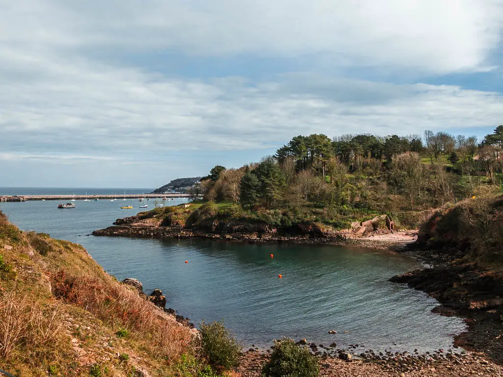 Looking down to the blue water in the cove, with a small secluded beach on the coastal walk from Paignton to Brixham.  There are lots of trees on the land surrounding the cove.