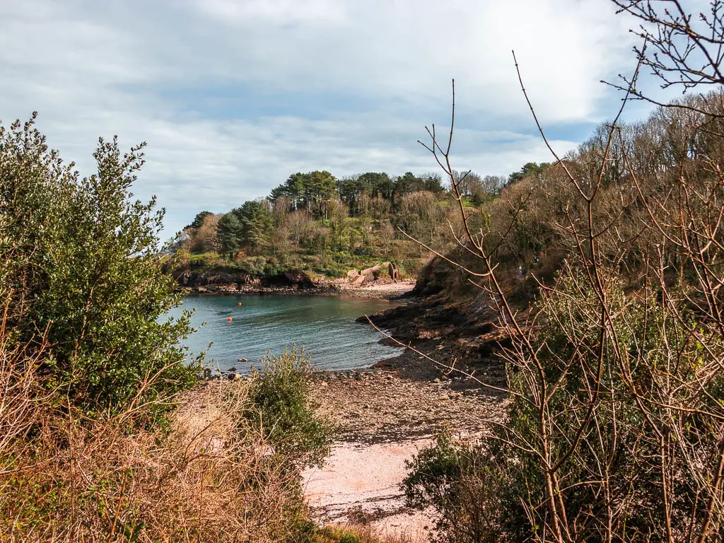 Looking through the trees towards the blue water of a secluded beach cove near the end of the walk from Paignton to Brixham.