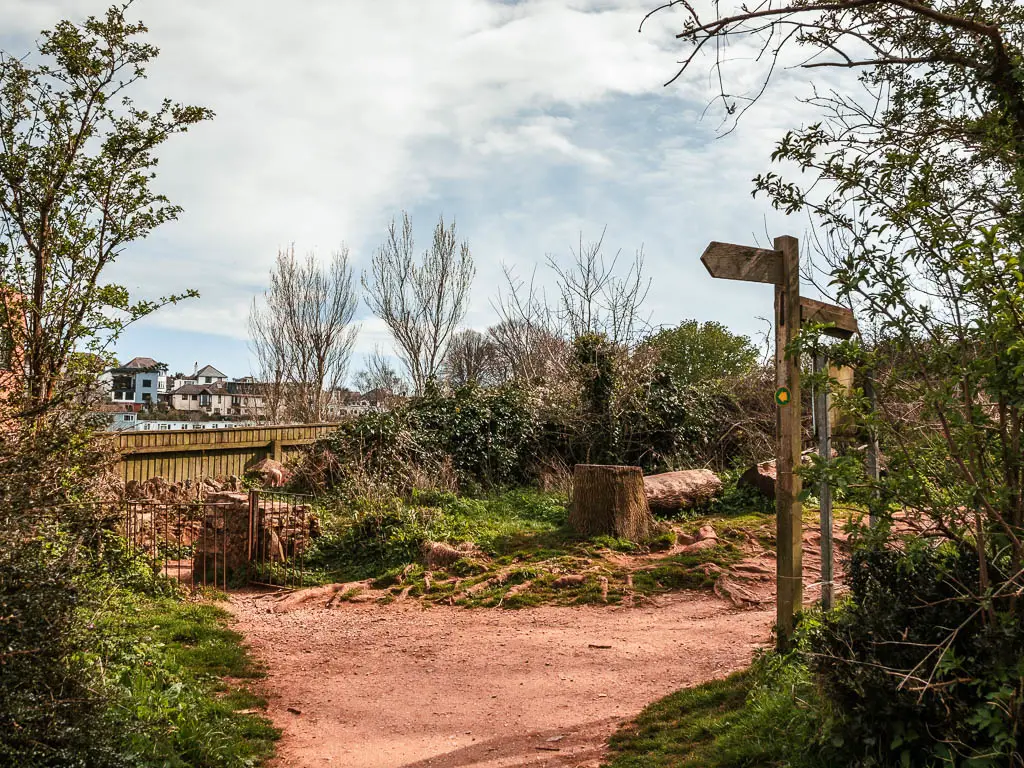 A path where it splits and a wooden trail signpost on the right.