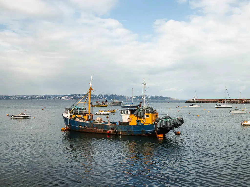 An old rusty looking shipping boat on the blue sea in Brixham at the end of the coastal walk from Paignton. 