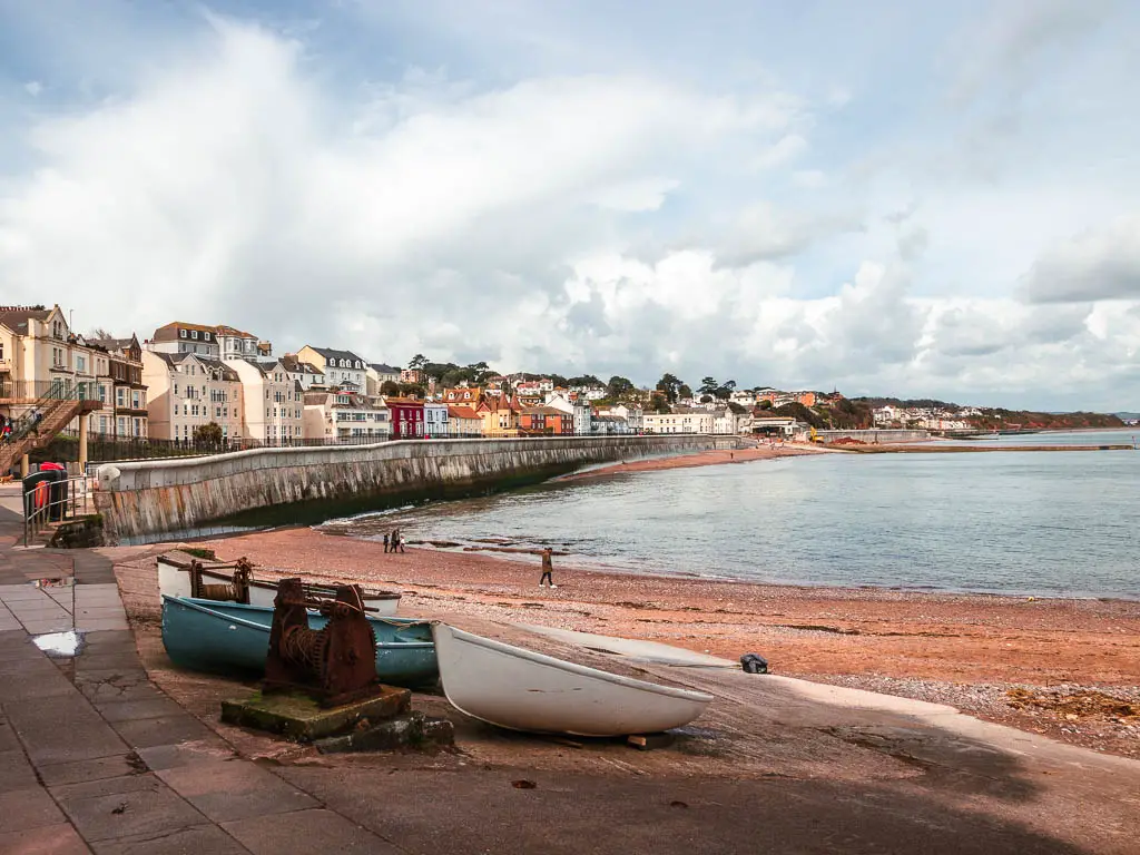 Looking across to the beach and sea, with a sea wall on the left and houses of Dawlish behind that on the walk from Teignmouth. There are a few rowboats on the ground next to the beach.