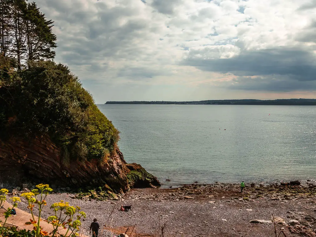 A small beach cove with grey pebbles and a small cliff on the left in Torquay, at the start of the coastal walk to Babbacombe.