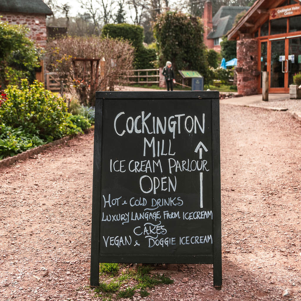 A black bored sign with white writing for the Cockington Mill.