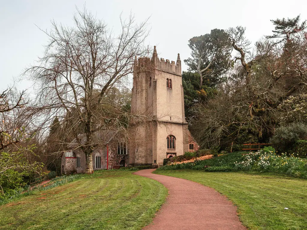 A covey path leading to a church in Cockington Park. The church is surrounded by a few leafless trees.