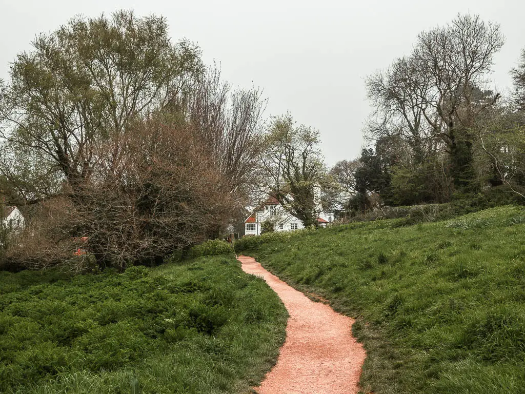 A trail running through the grass on the walk back to Torquay from Cockington. There are some leafless trees on the other side and a white coloured house at the end of the trail.