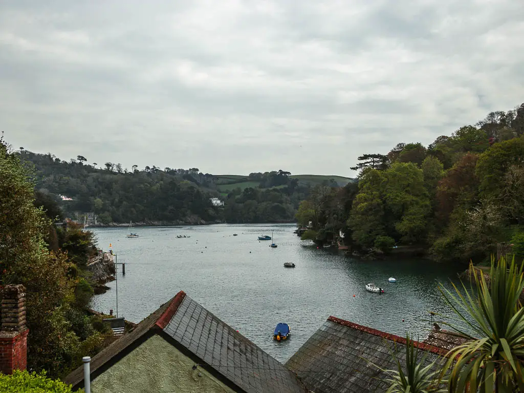 Looking across the rooftops to the river dart. There are a few boats dotted about the river. the river is lined with lots of trees. 