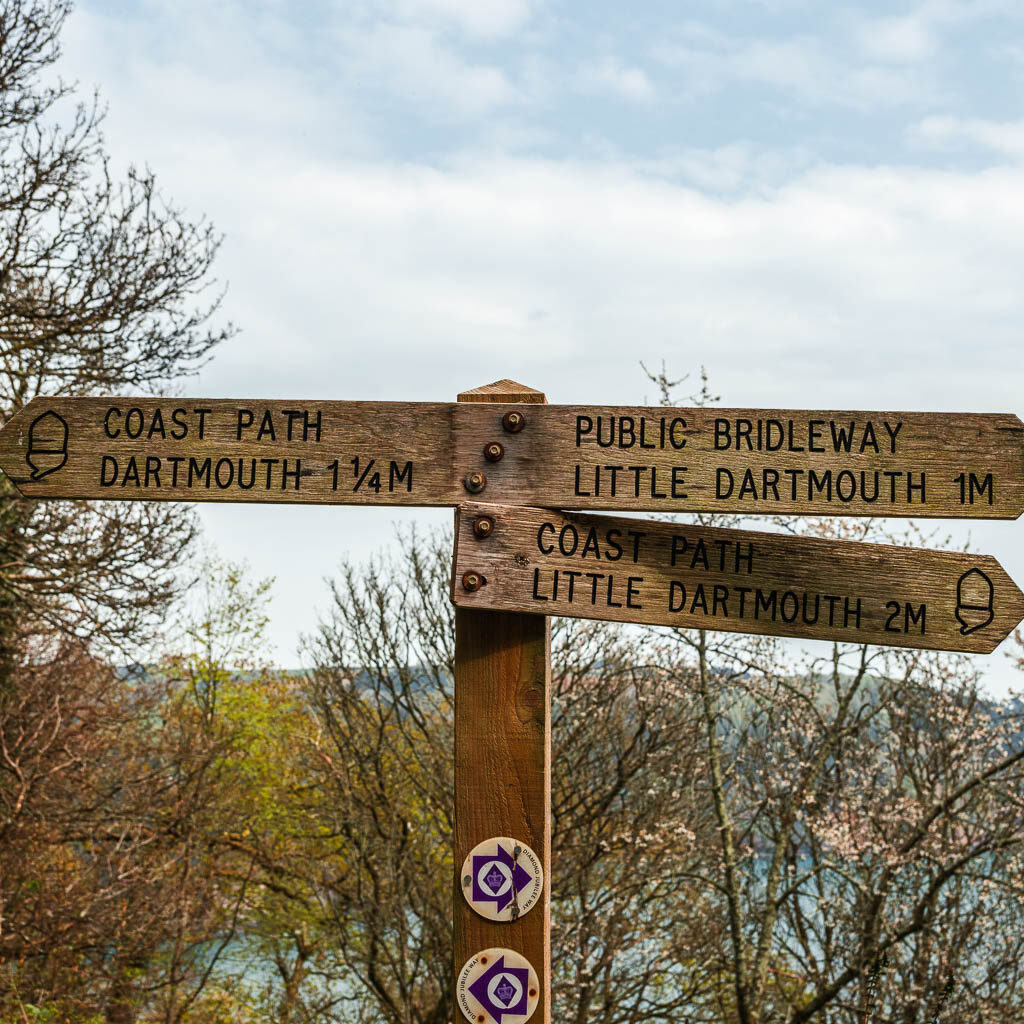 A wooden multi junction trail signpost pointing to Dartmouth and little Dartmouth on the walk towards Blackpool Sands. 