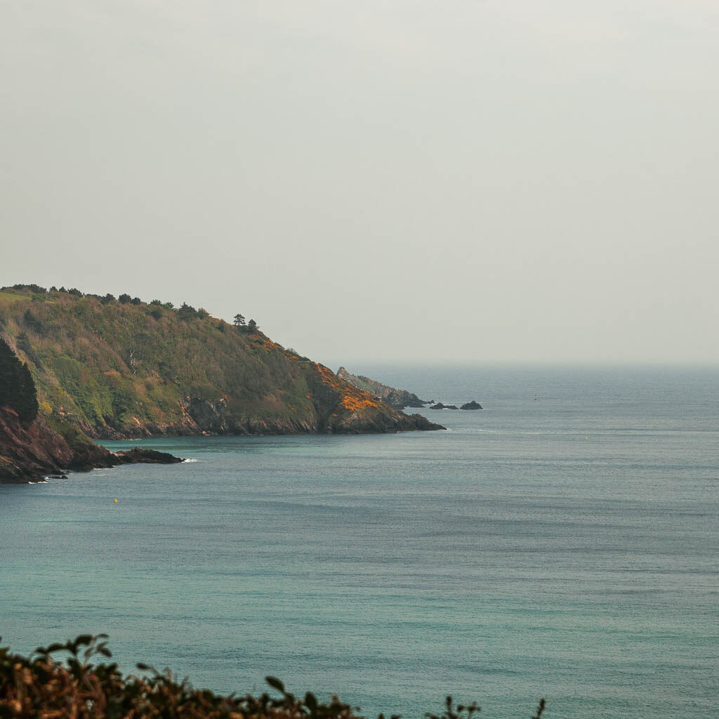 Looking across the blue sea to a tree covered cliff peninsular. 