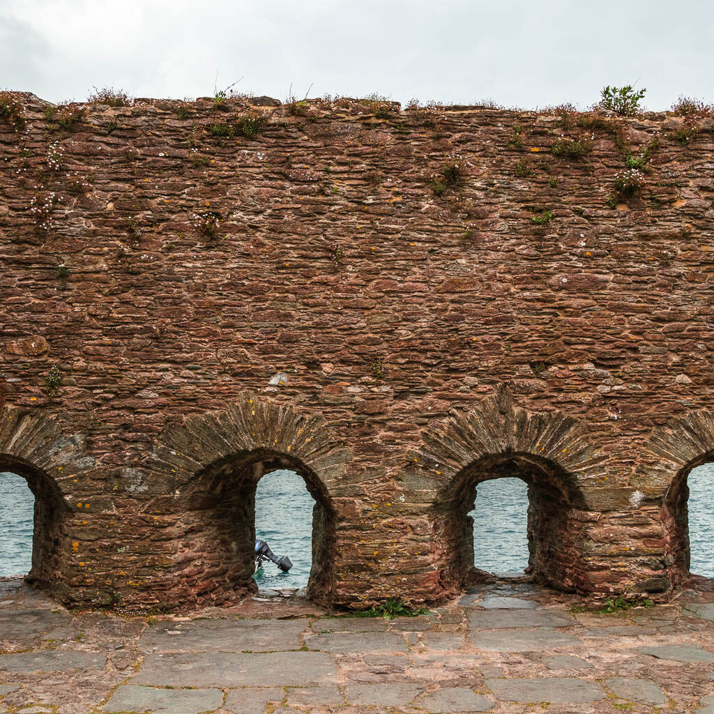 A stone wall with arch holes looking through to the river.