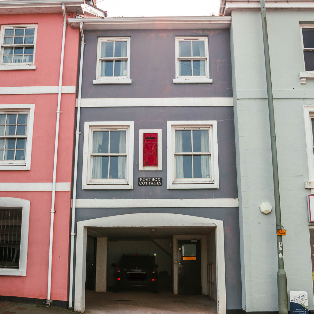 A red post box up on the first floor of a pastel coloured building in stoke flemming, along the coastal walk from Dartmouth to Blackpool Sands.