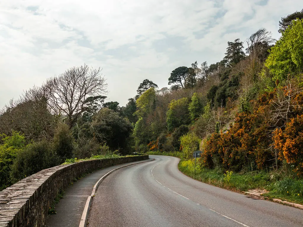 A winding road, with a low stone and brick wall on the left and trees and bushes on the right, near the end of the Dartmouth to Blackpool Sands walk.