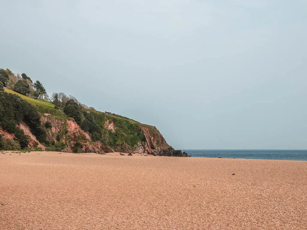 Looking across Blackpool sands beach at the end of the walk from Dartmouth. There are cliffs to the left, and the blue sea ahead. 