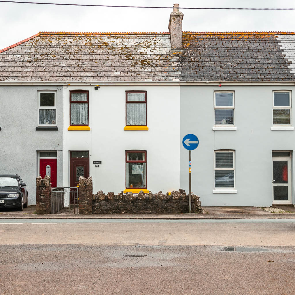 Houses with grey and white facades across the road, with a blue direction signpost.