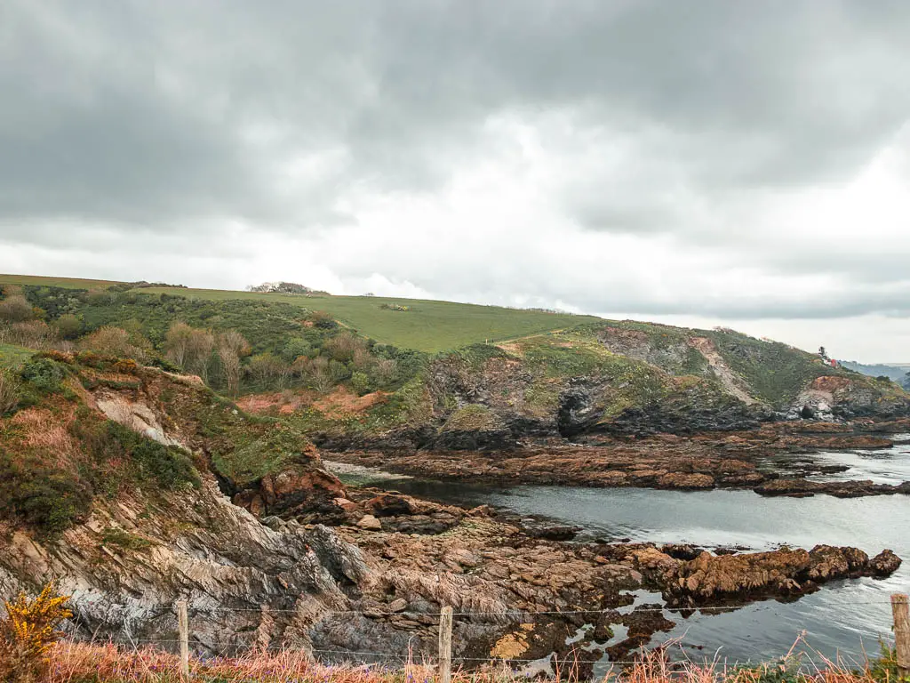 Looking towards a very rocky and cliffy beach cove with grass covered clifftops, and the sea to the right near the end of the walk from Par to Fowey.