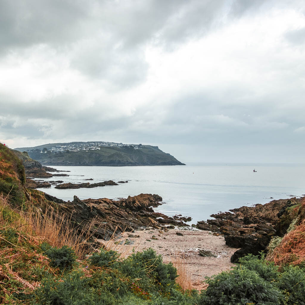 Looking across the small sandy beach cove to the sea ahead and the peninsular of polruan in the distance. 