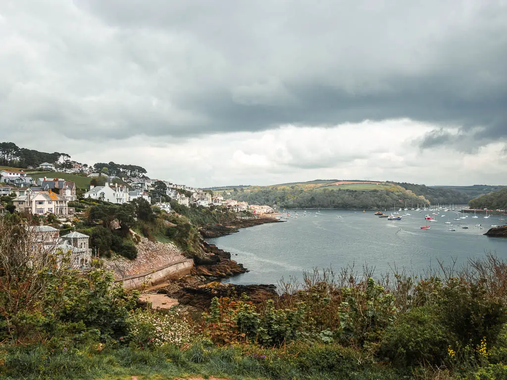 Looking down towards the harbour of Fowey, at the end of the coastal walk from Par. There are lots of buildings on the cliff coastline on the left and lots of boats in the water ahead. 