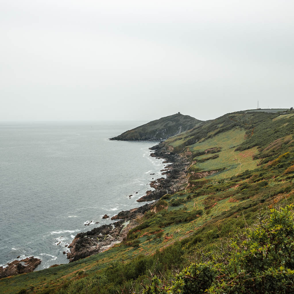 Looking along the rocky coastline as it leads to a grass covered slope uphill. 