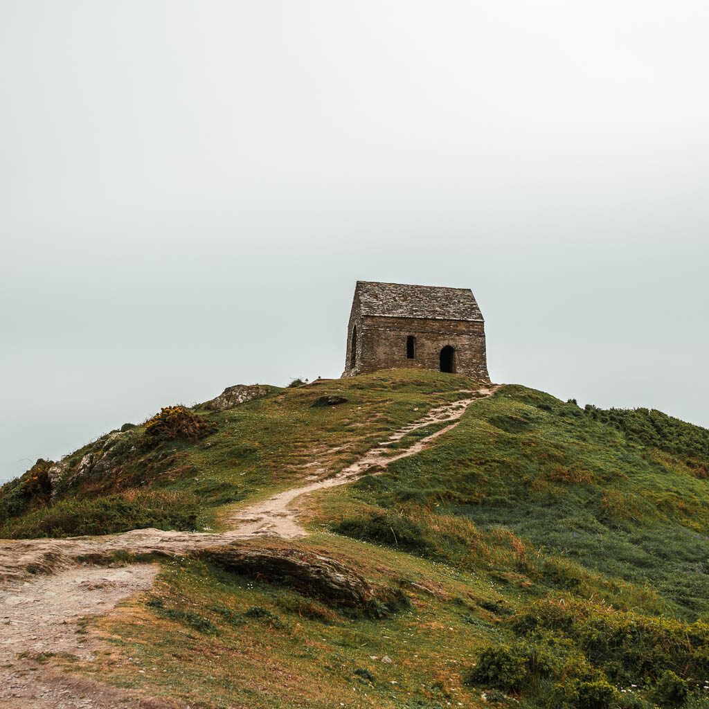 A trail leading up a green hill towards a small abandoned church building.