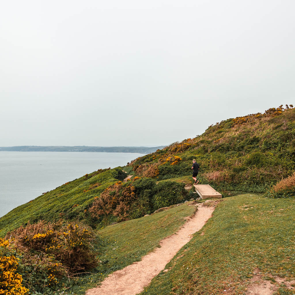 A trail running along the hillside. There is a man walking ahead on the trail.