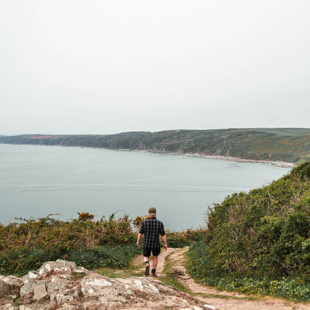 A man walking down over some rocks with a view out to the sea ahead. 