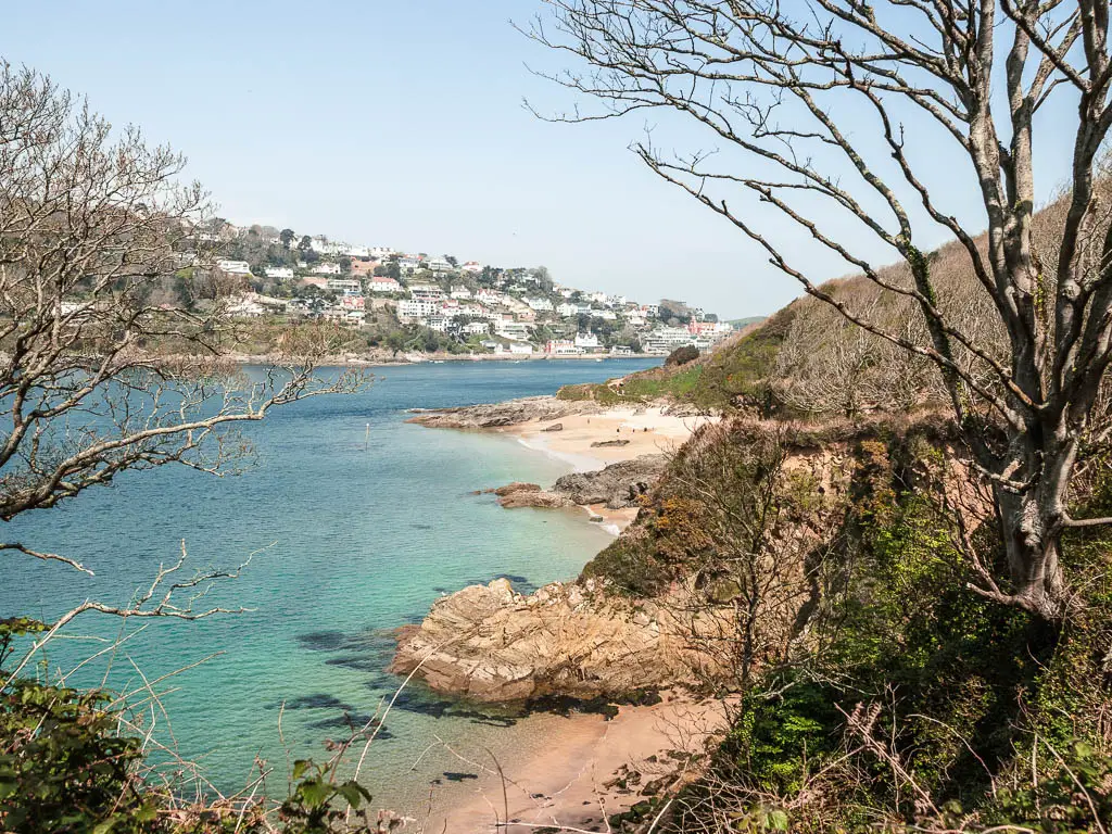Looking through a gap in the trees to the light blue turquoise see, and two small sandy beach coves within the cliffs.