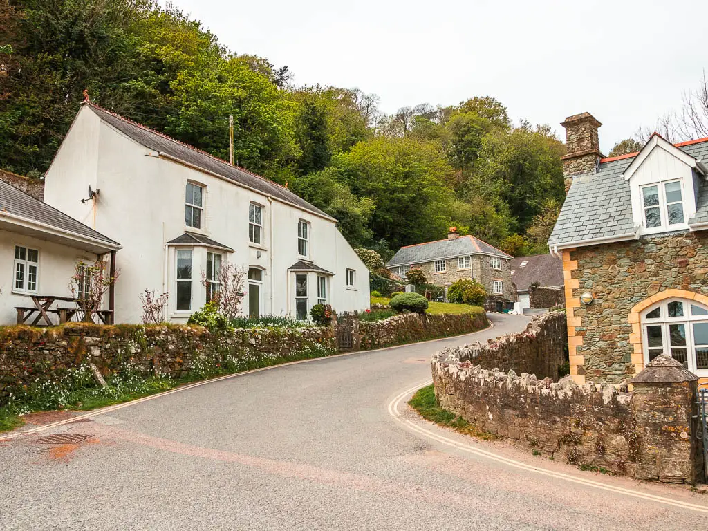 A road circling uphill to the right, lined with a stone wall on both sides, with houses behind the walls.